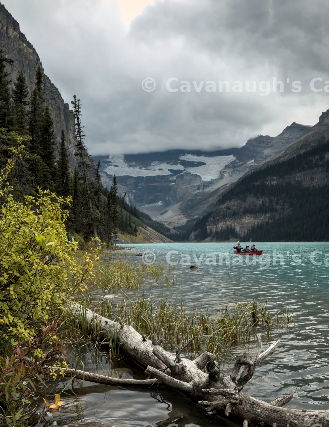 Canoeists paddling turquoise Lake Louise with a glacier and storm clouds over the mountains behind